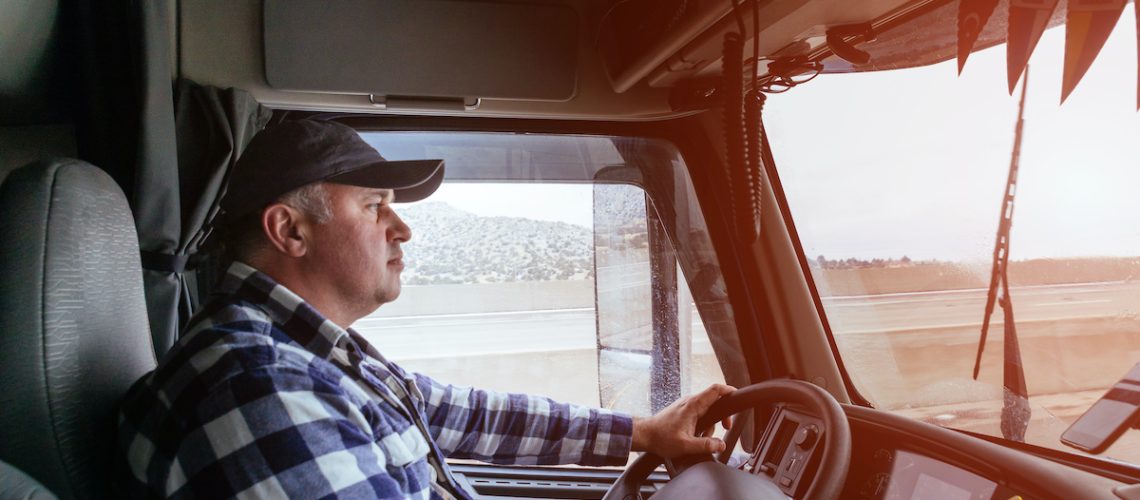 Driver in cabin of big modern truck vehicle on highway